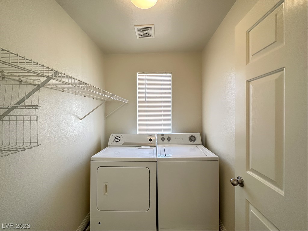 Laundry room with a white washer and dryer beneath a window, with wire shelving along the wall.