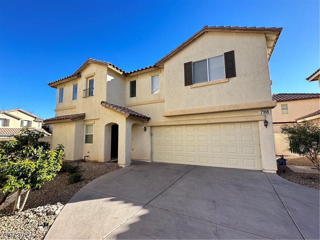 Two-story stucco house with a double garage, arched entry, and gravel landscaping.