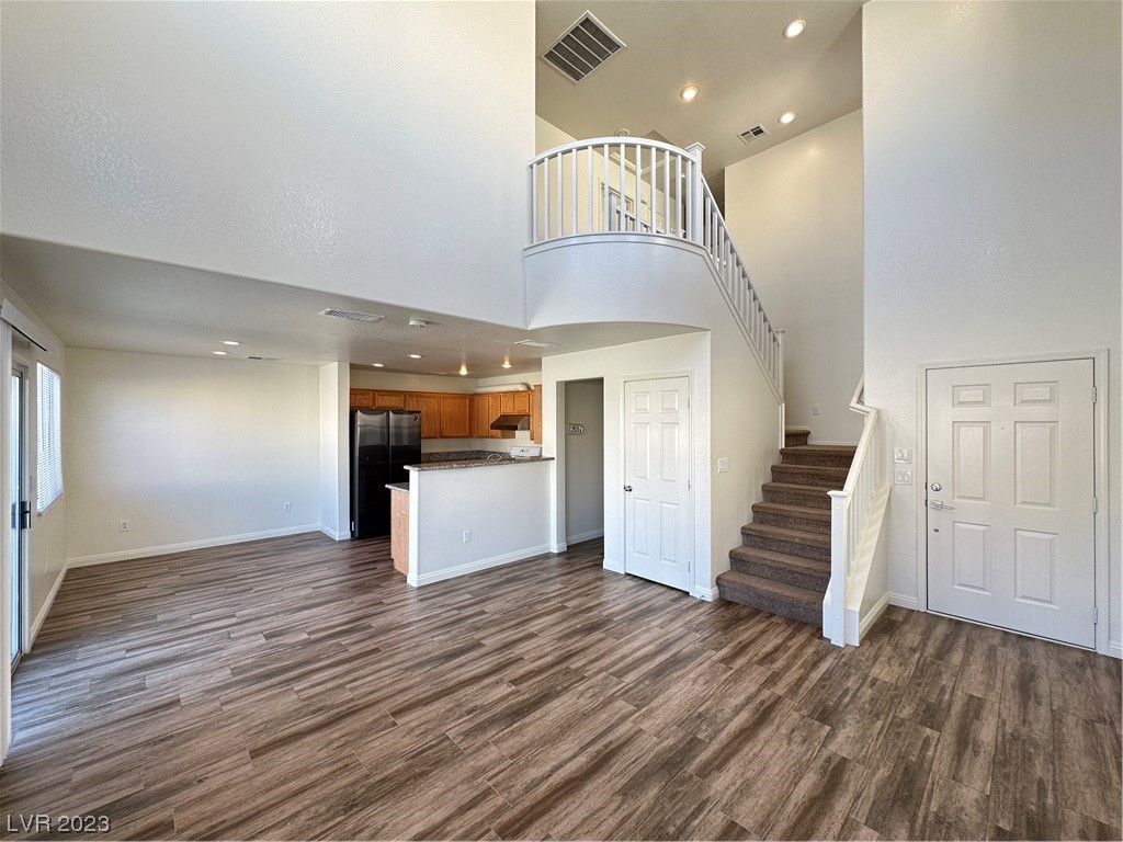 Unfurnished open-plan living area with wood-look floors, kitchen breakfast bar, and carpeted staircase.