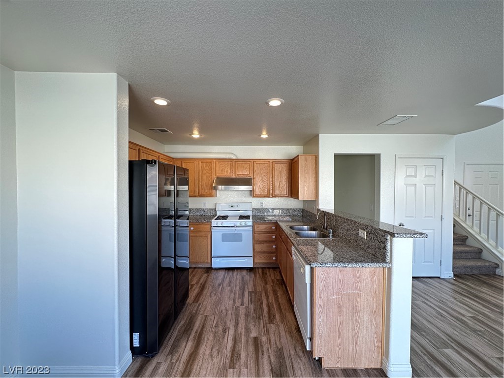 Kitchen with wood cabinets, granite counters, a double-sink peninsula, and wood-look flooring.
