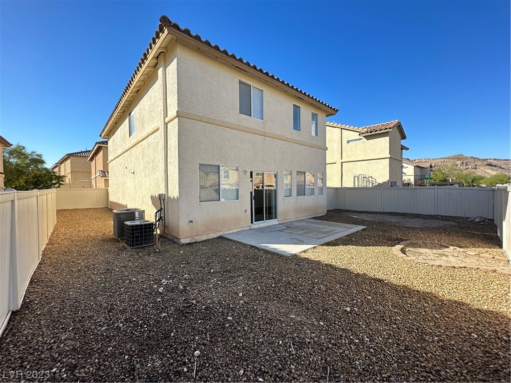 Back of a two-story stucco home with a concrete patio and gravel yard.