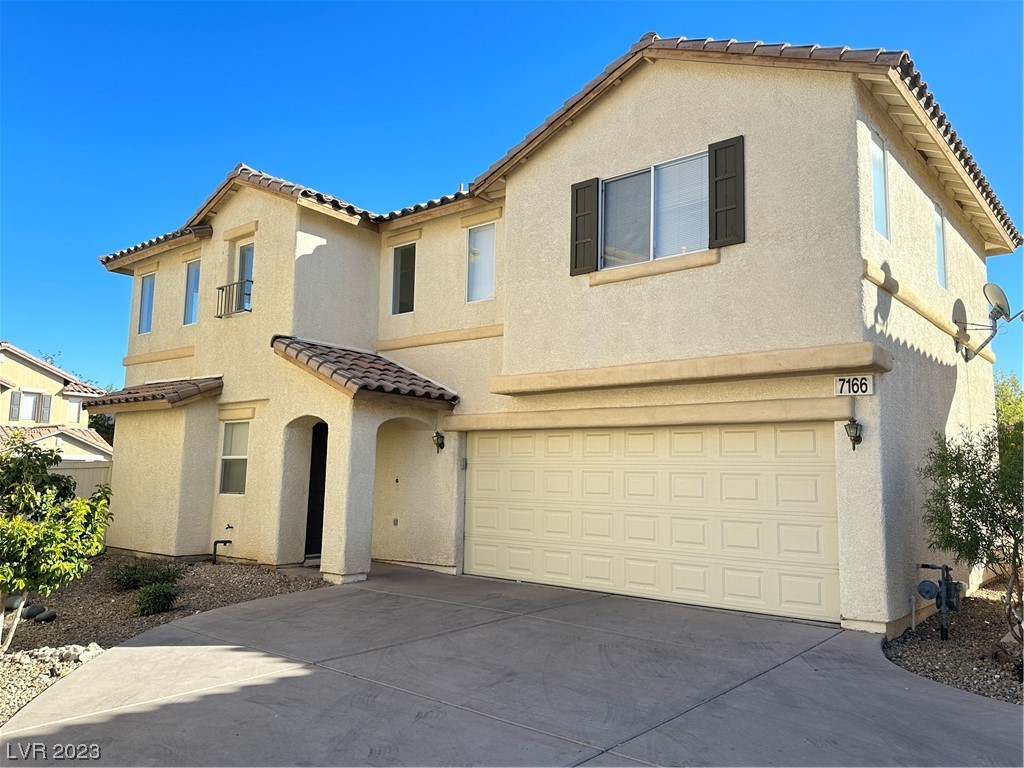Two-story beige stucco home with a tiled roof, arched entry, and wide two-car garage.