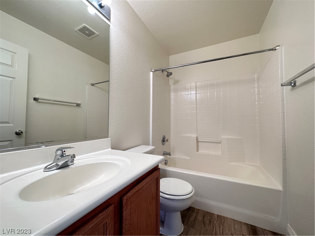 Bathroom with a white tub and tiled surround, vanity sink, dark wood cabinet, and large mirror.