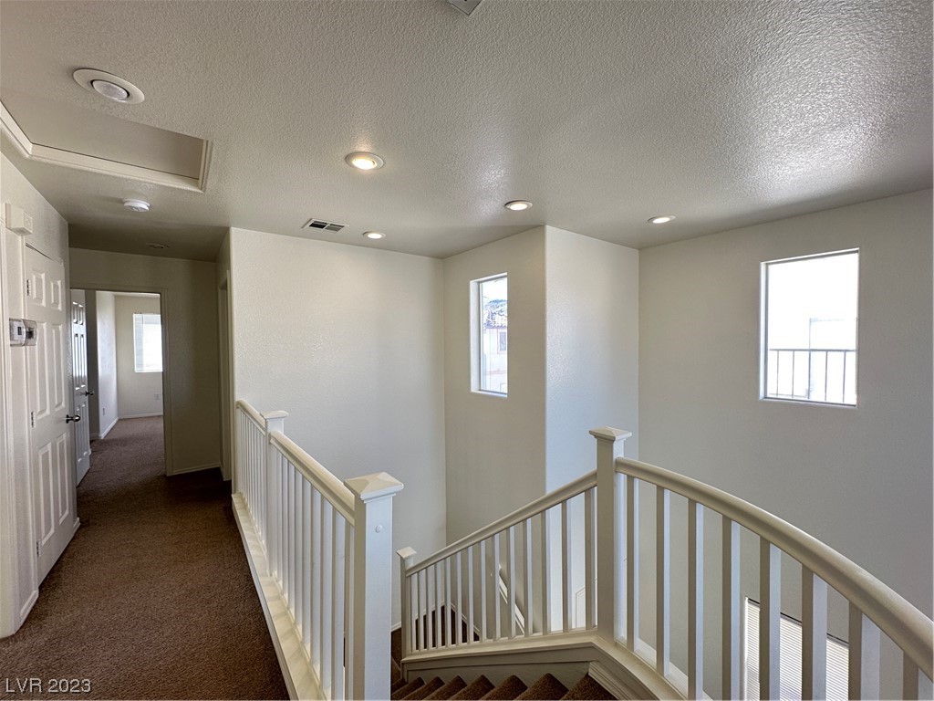 Upstairs landing with beige carpet, white stair railings, recessed lights, and two windows.