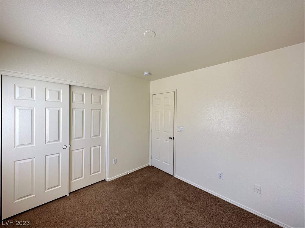 Empty bedroom with brown carpet, sliding closet doors, and a separate hinged door.