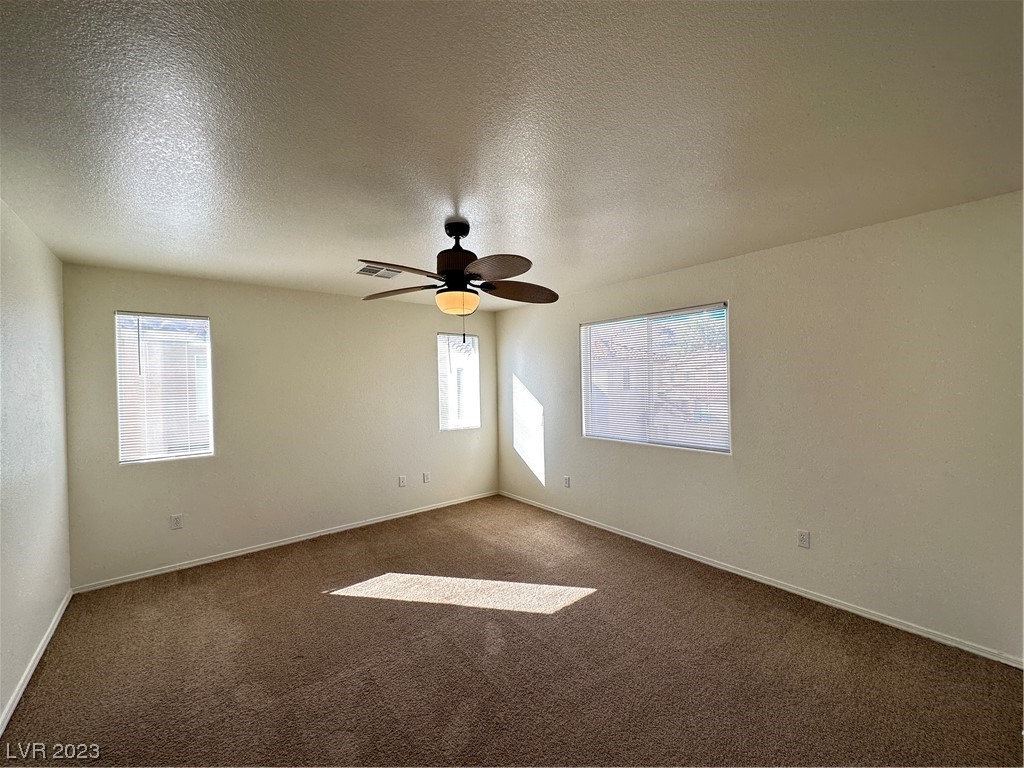 Empty bedroom with brown carpet, three windows, and a ceiling fan with light.