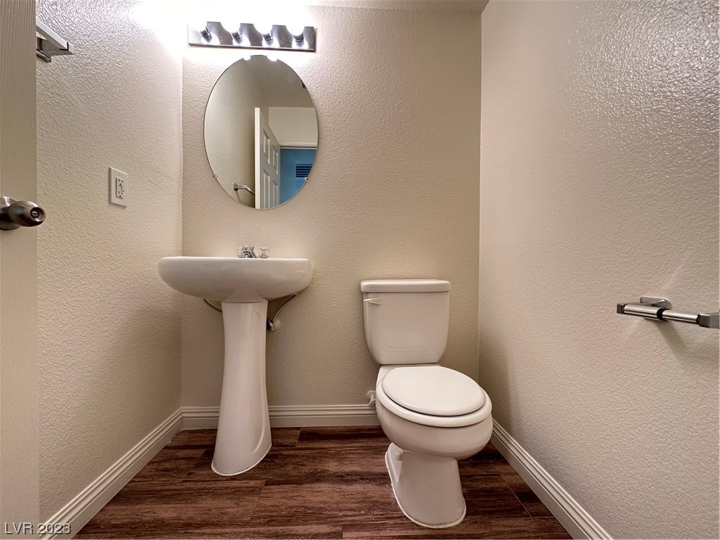Bathroom with a white pedestal sink, toilet, oval mirror, and dark wood-look flooring.