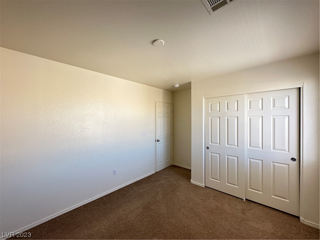 Empty bedroom with beige carpet and white sliding closet doors.