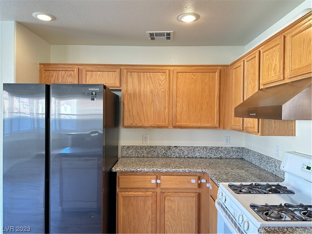 Kitchen with oak cabinets, granite counters, a black refrigerator, and a white gas range.