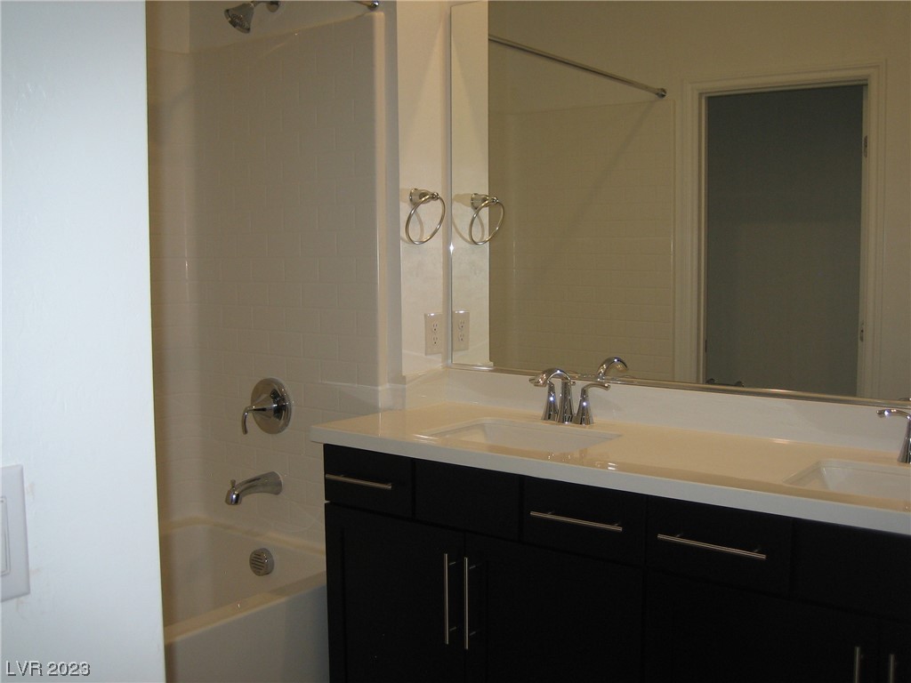 Bathroom with a double-sink vanity, dark cabinetry, large mirror, and adjacent tub-shower.