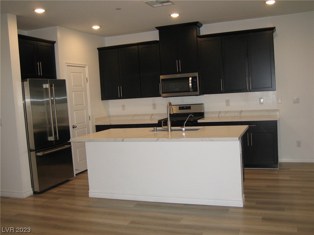 Kitchen with dark cabinets, stainless steel appliances, and a large island with a sink.