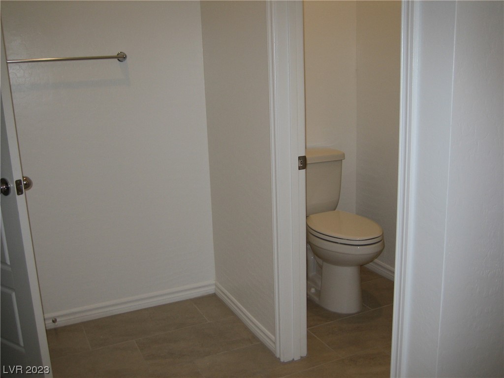 Bathroom with a toilet in a separate alcove, tile flooring, and a wall-mounted towel bar.