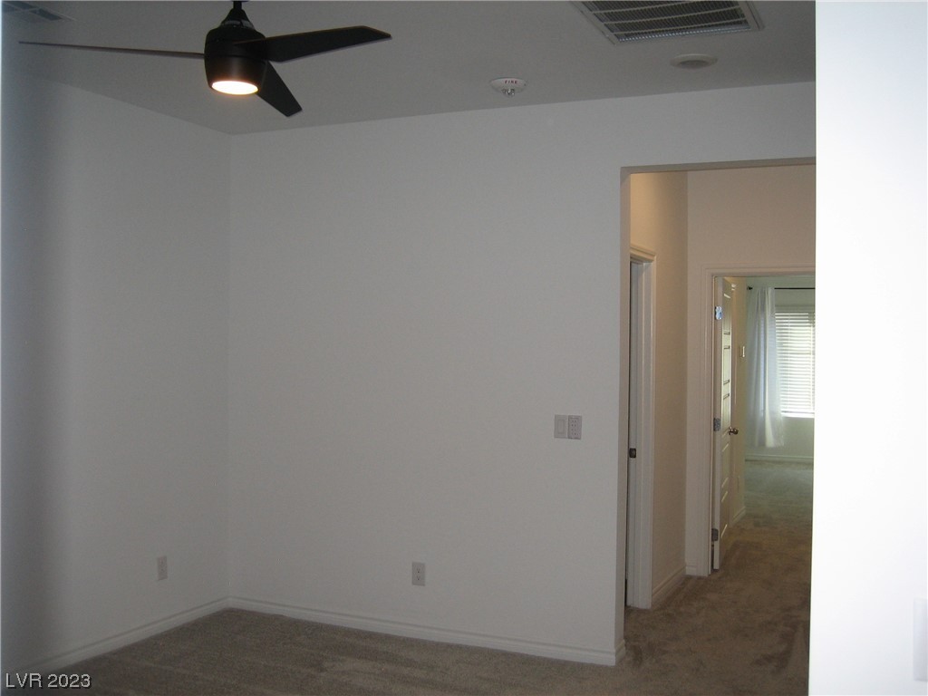Empty carpeted room with a black ceiling fan and an open doorway to the hall.