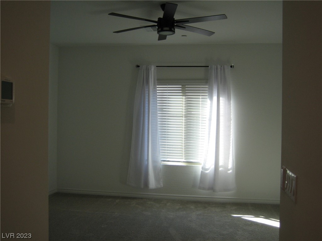 Vacant carpeted bedroom with a ceiling fan and a bright window with blinds.