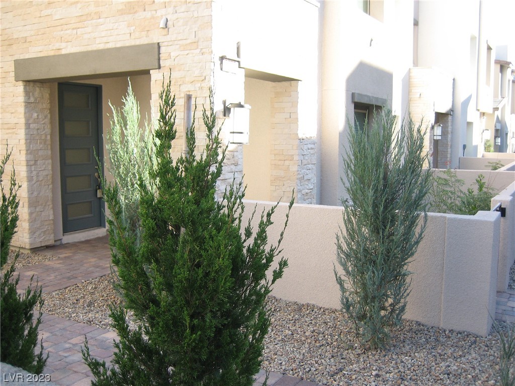 Residence entrance with a dark front door, stone facade, paved walkway, and gravel landscaping.