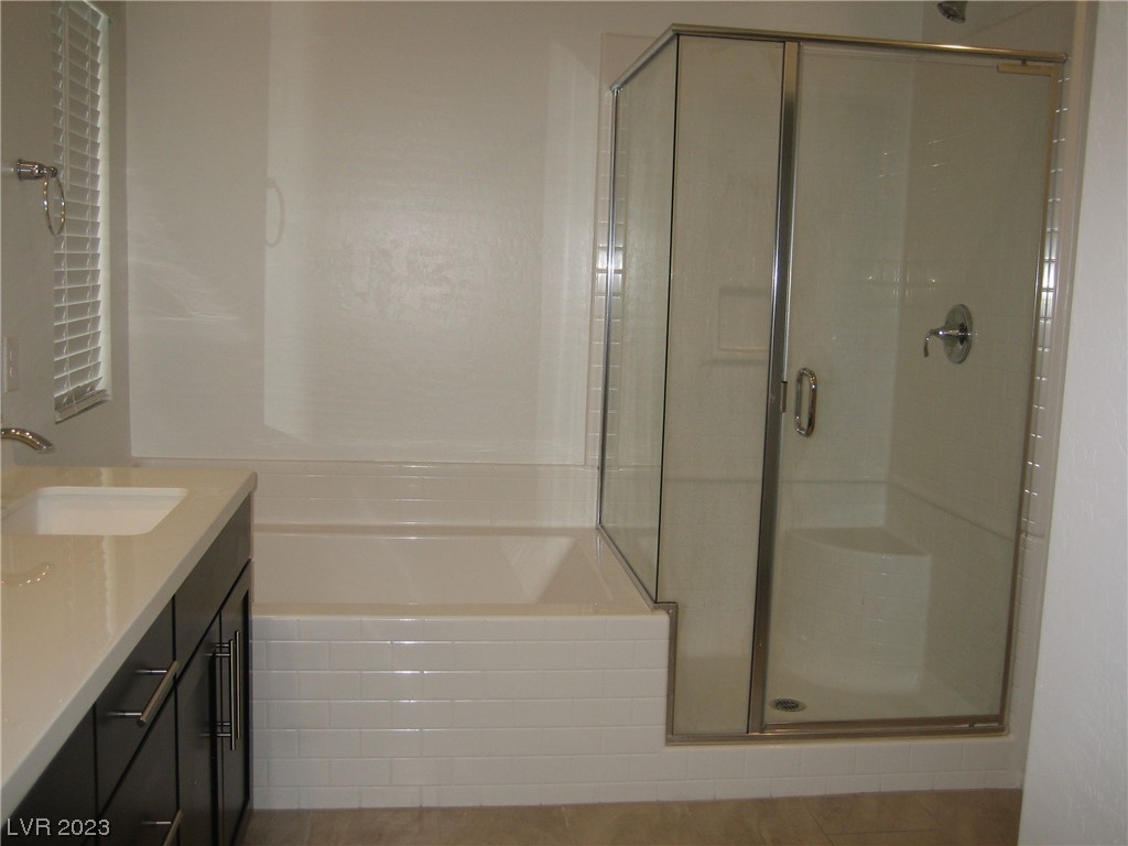 Bathroom with a tiled bathtub, glass shower, dark vanity, and window blinds.