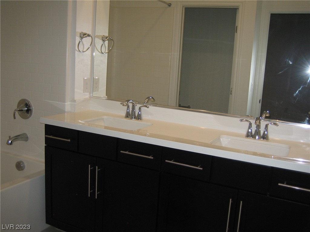 Bathroom with a double-sink vanity, dark cabinets, and a white-tiled bathtub.