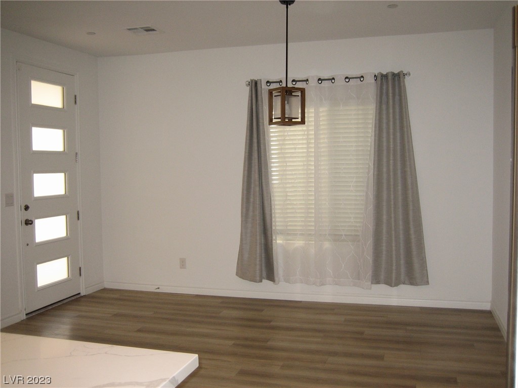 Empty interior room with wood-look floors, a curtained window, and a front door with frosted glass panels.