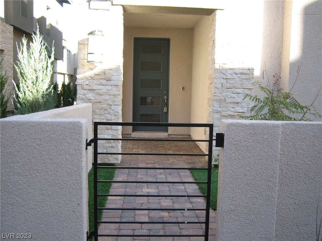 Front entry with a black metal gate, paver walkway, stone accents, and dark paneled door.