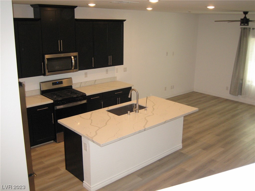 Vacant kitchen with dark cabinetry, stainless appliances, and a veined quartz island with sink.