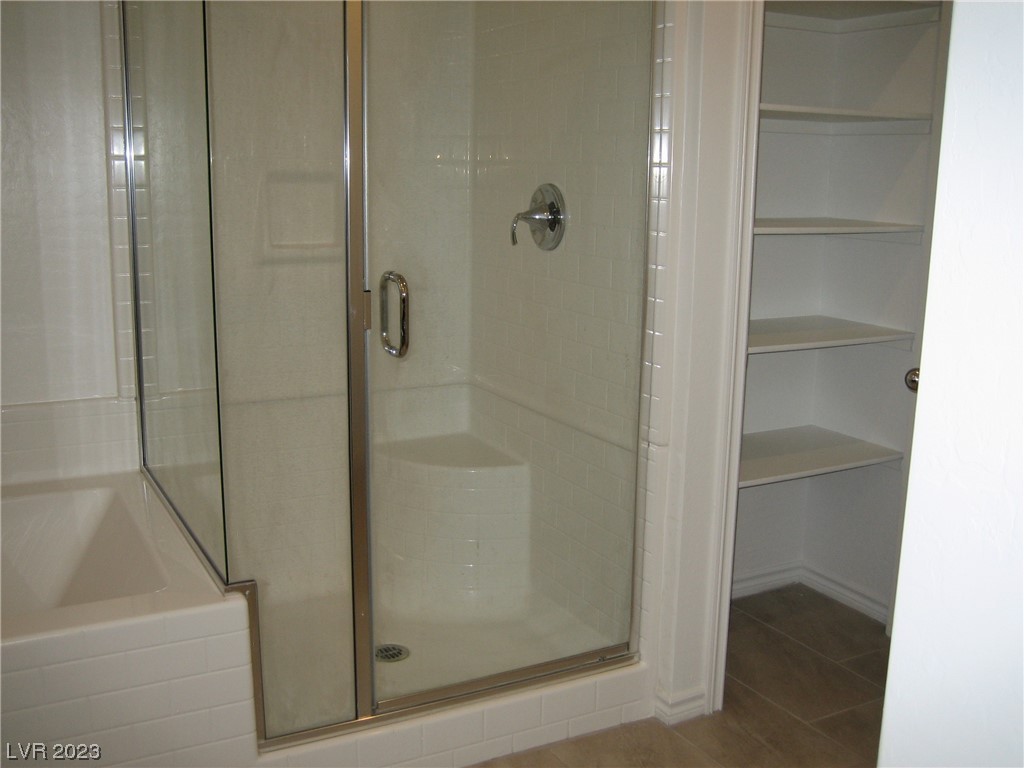 Bathroom with glass-enclosed tiled shower, adjacent bathtub, and open built-in shelves.