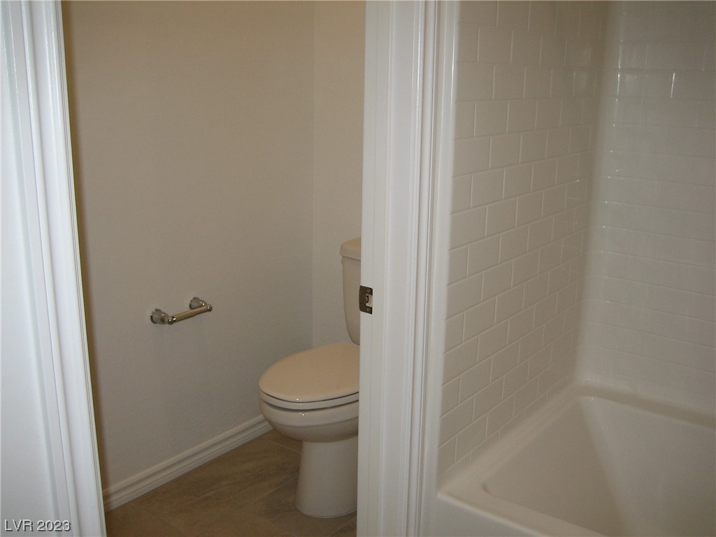 Bathroom with a white toilet beside a tub and white subway-tile walls.
