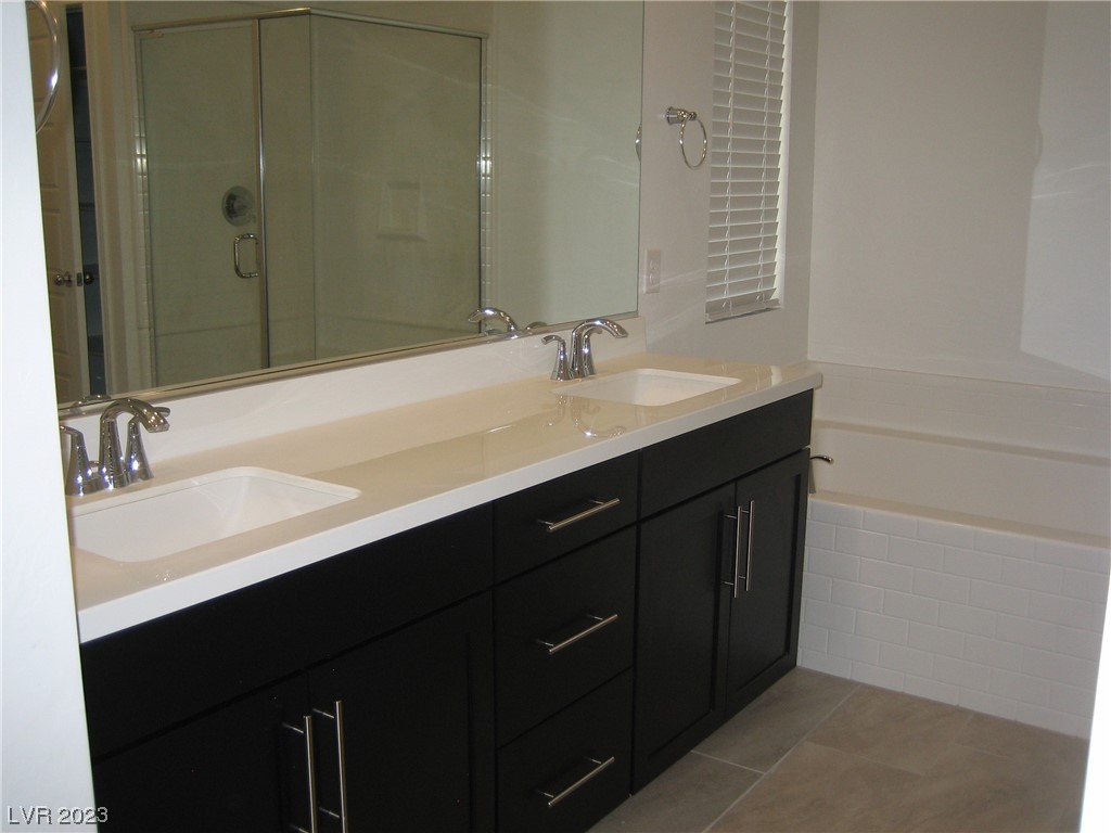 Bathroom with double sinks, dark vanity cabinetry, a large mirror, and a white bathtub.
