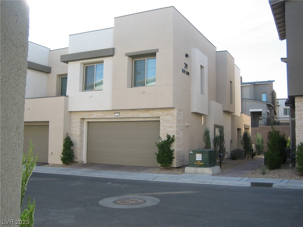 Two-story beige townhouse with a stone-trimmed garage and desert landscaping along a residential lane.