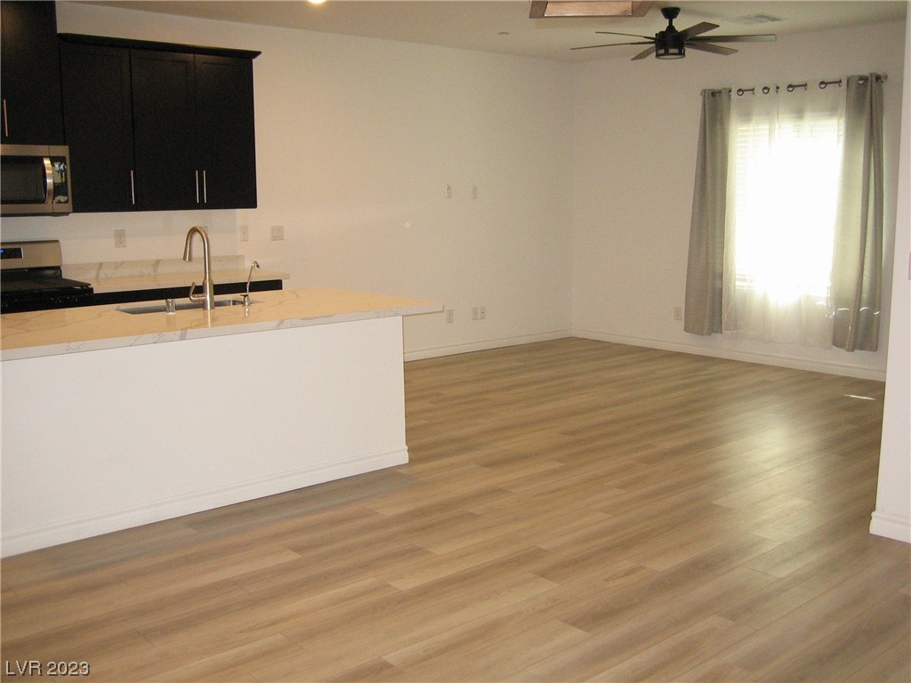 Open-plan kitchen and living area with a white peninsula, dark cabinets, and wood-look flooring.