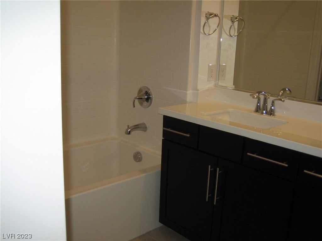 Bathroom with a white bathtub beside a dark vanity and mirrored backsplash.