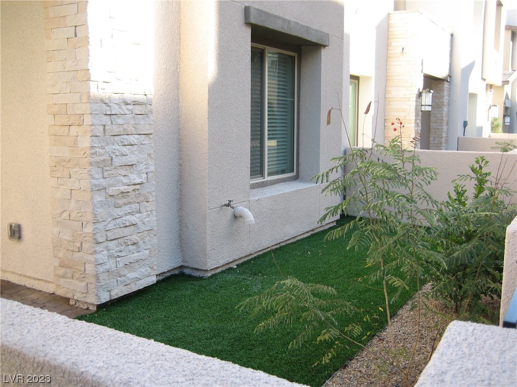 Stucco residence with stone accents beside a narrow lawn and landscaped courtyard.