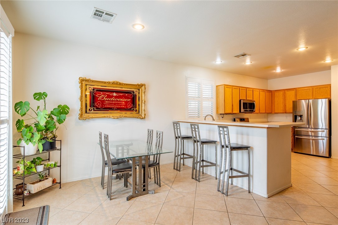 Open kitchen and dining area with a breakfast bar, wood cabinets, stainless appliances, and glass dining table.