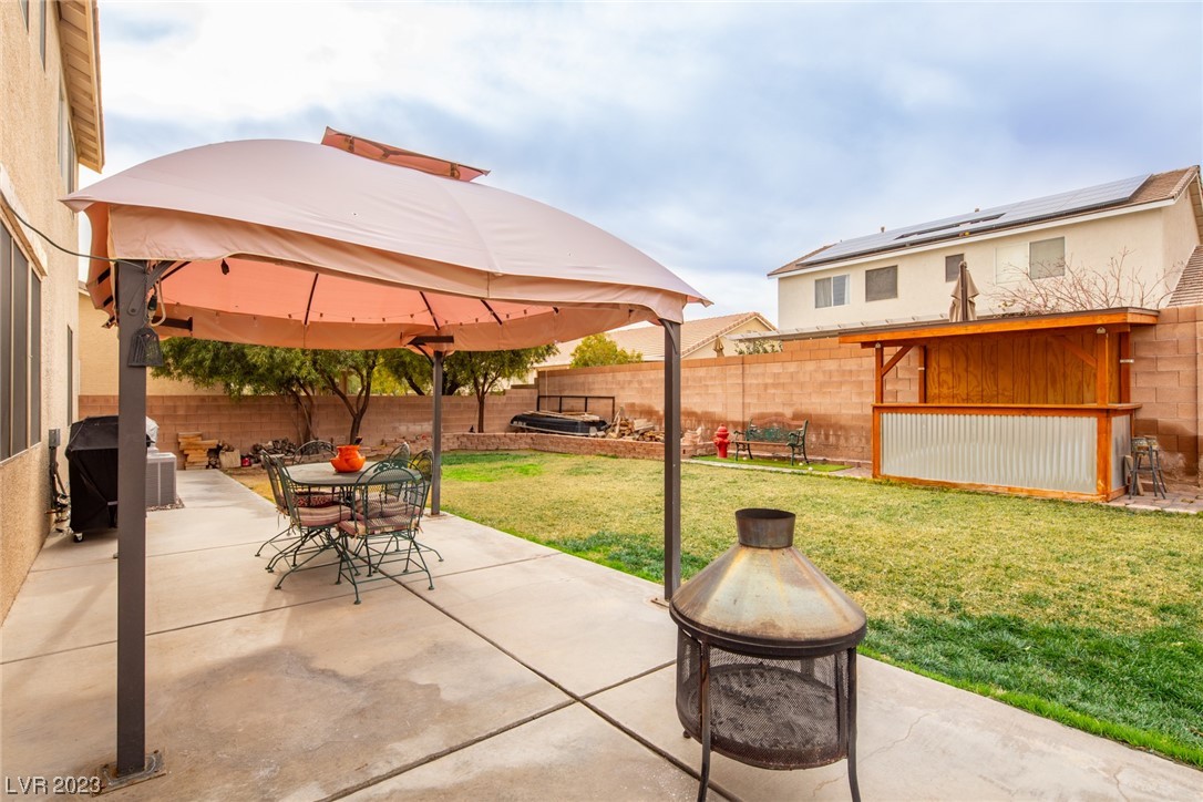 Backyard patio with a shade canopy, outdoor dining set, chiminea, and covered wooden bar.