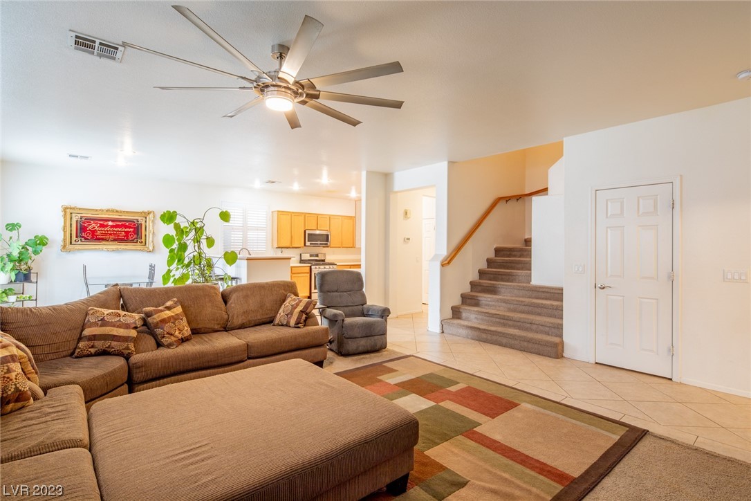 Furnished living room with brown sectional, colorful rug, ceiling fan, and staircase beside the kitchen.