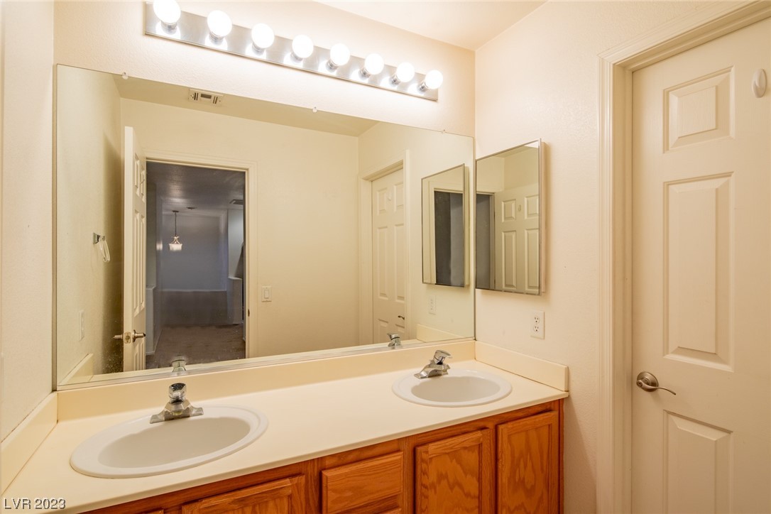 Bathroom with a double-sink vanity, large mirror, bright lights, and warm wood cabinets.