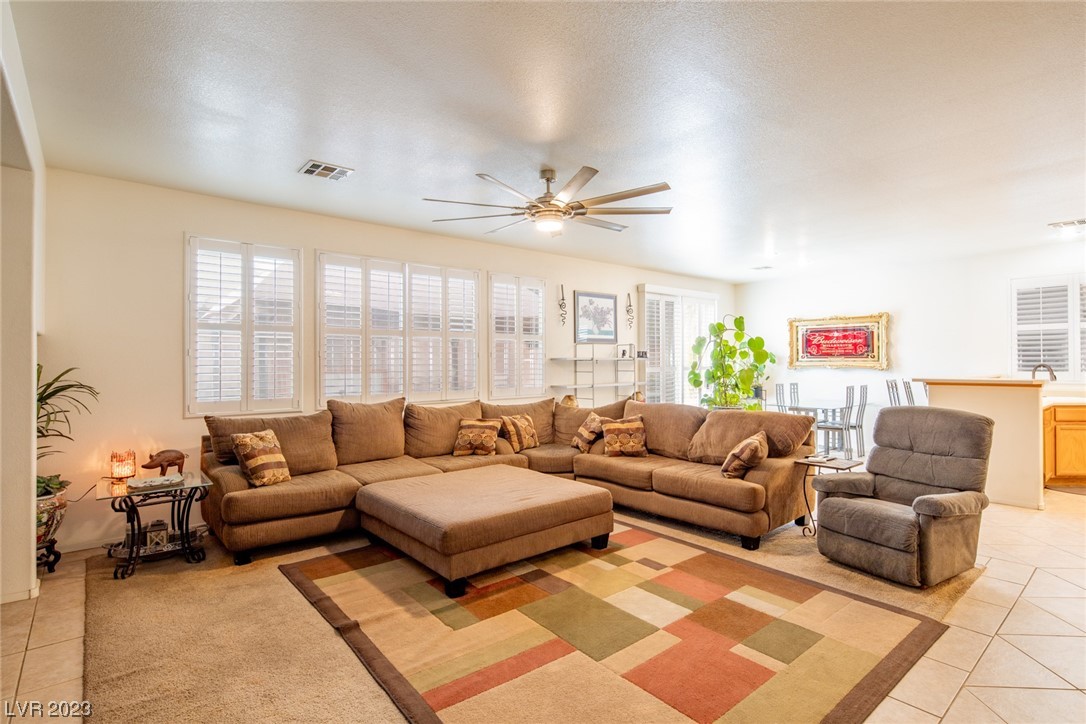 Furnished living room with a brown sectional, recliner, colorful rug, and plantation shutters.