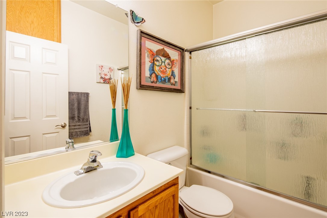 Bathroom with a wooden vanity, bathtub with frosted glass doors, and colorful framed artwork.