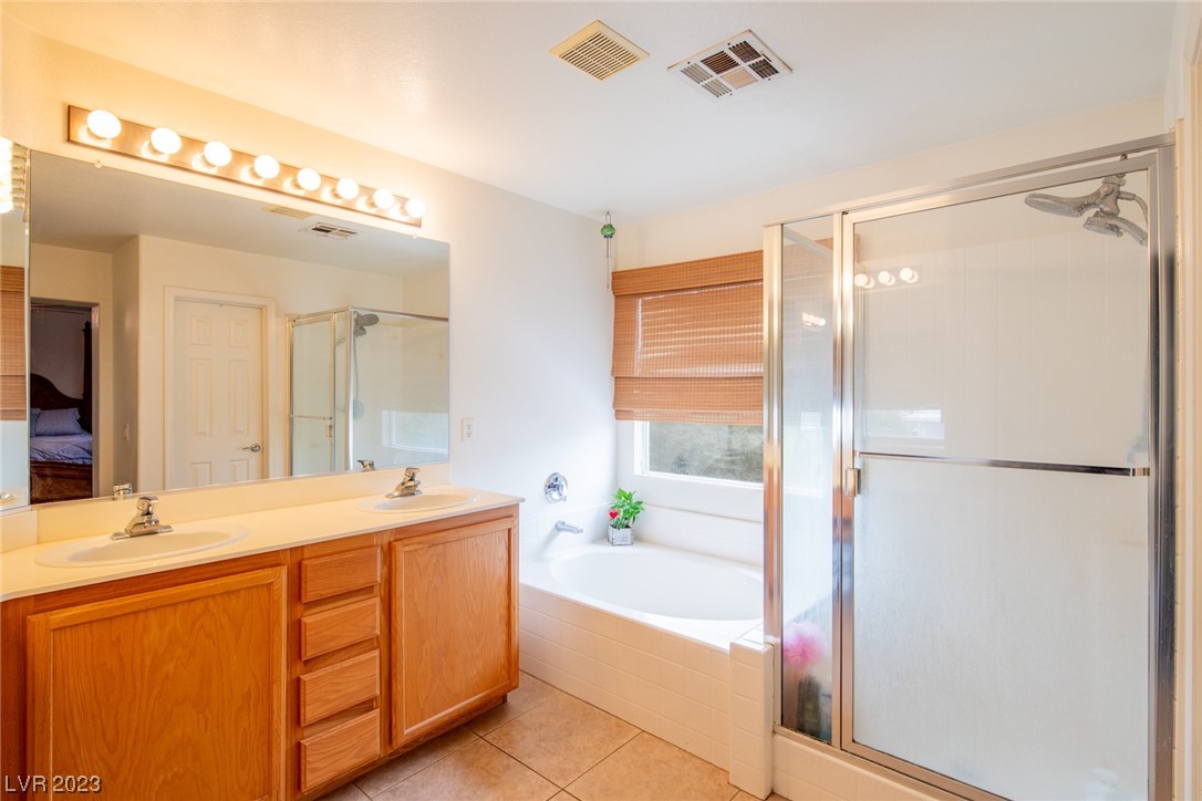 Bathroom with a double-sink wood vanity, bathtub beneath a window, and separate glass shower.