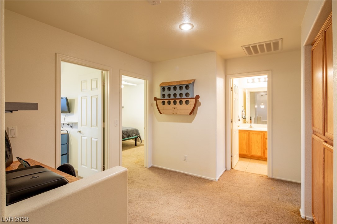 Carpeted room with a desk, a bedroom doorway, a bathroom doorway, and a wooden wall-mounted game rack.