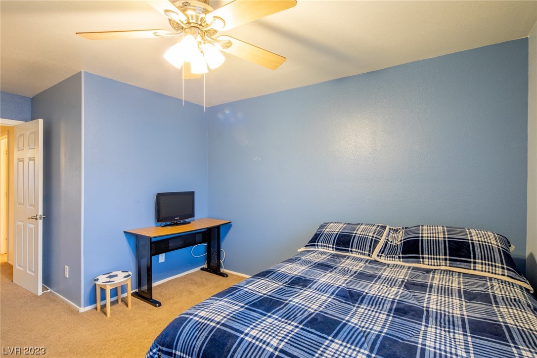 Bedroom with blue walls, plaid bedding, a ceiling fan, and a desk with a television.