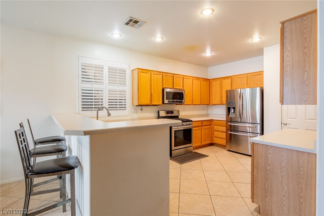 Kitchen with honey-colored cabinets, stainless steel appliances, and a peninsula breakfast bar with stools.