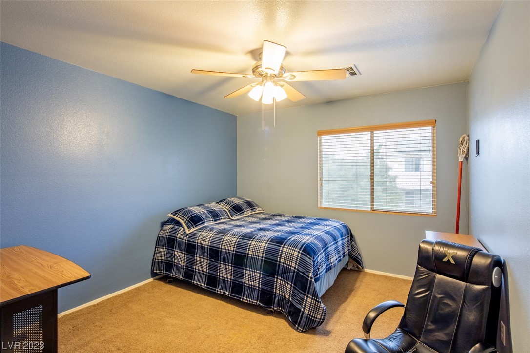 Bedroom with blue plaid bedding, blue walls, and a ceiling fan with light.