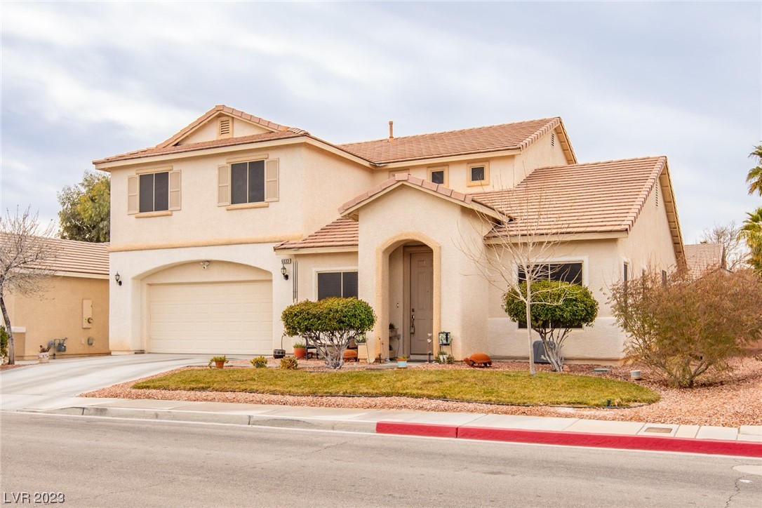 Two-story beige stucco home with a tile roof, attached garage, and desert landscaping.