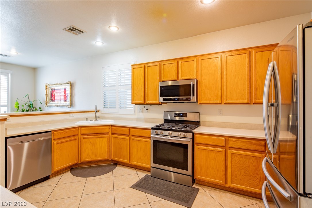 Kitchen with honey-colored cabinets, stainless steel appliances, and a sink beneath shuttered windows.