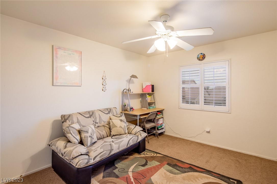 Furnished den with a patterned futon, compact desk, and plantation-shuttered window.
