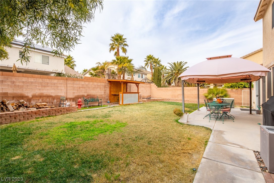 Backyard with a lawn, patio dining set beneath a canopy, wooden outdoor bar, and firewood storage.