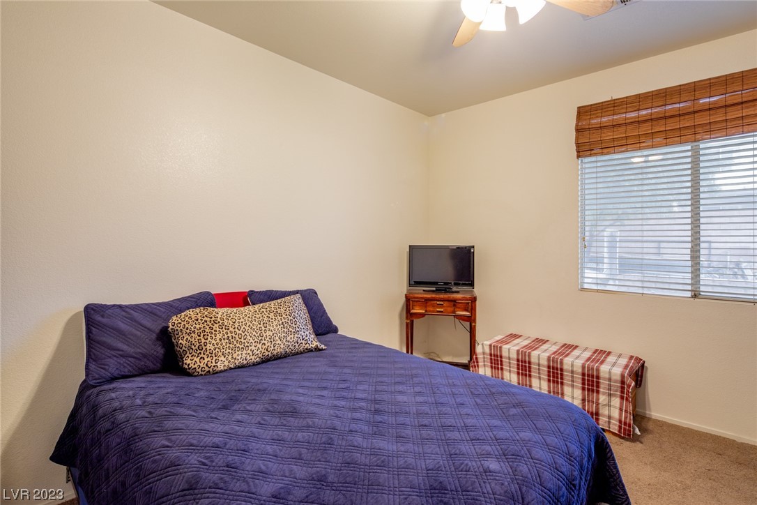 Bedroom with a dark blue quilted bed, television on a wooden table, and window with bamboo shade.