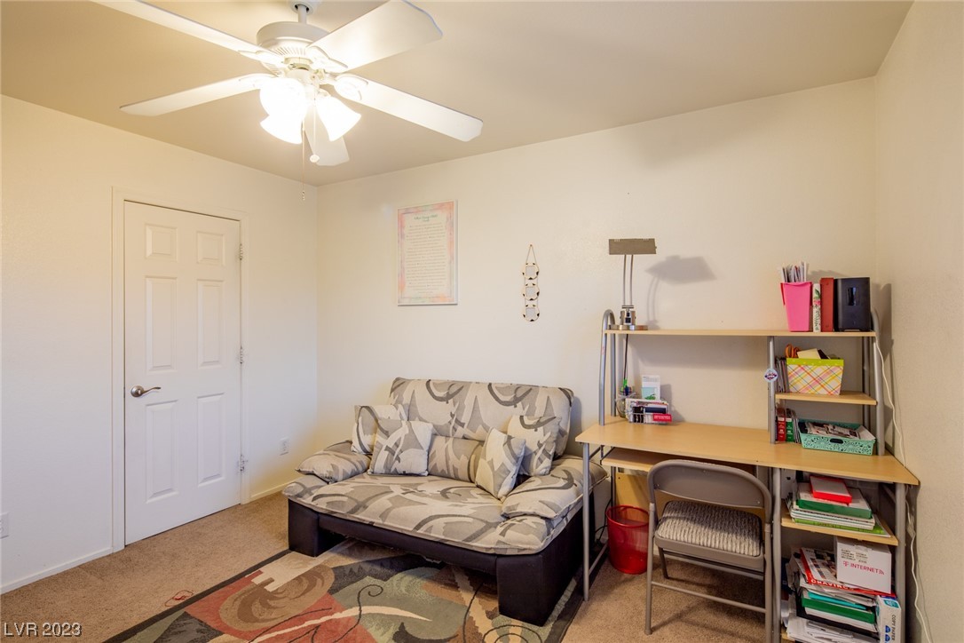 Furnished office with a patterned futon, desk and shelving, and ceiling fan with lights.
