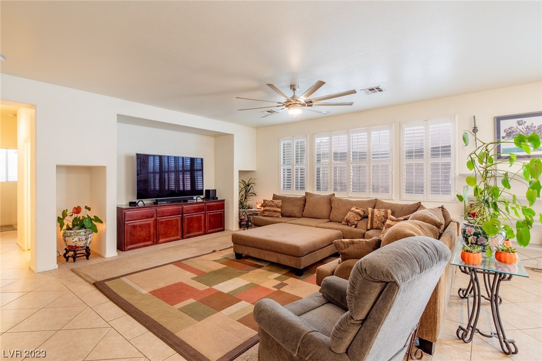 Furnished living room with a sectional sofa, colorful geometric rug, shuttered windows, and ceiling fan.
