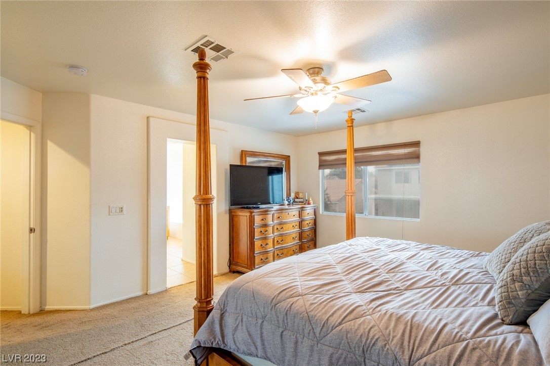 Bedroom with a wooden four-poster bed, gray quilt, and dresser beneath a ceiling fan.